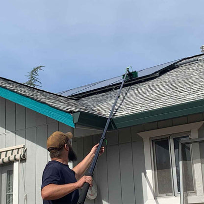 A man using the extended water fed pole to clean a solar panel on a roof, demonstrating its reach and effectiveness.