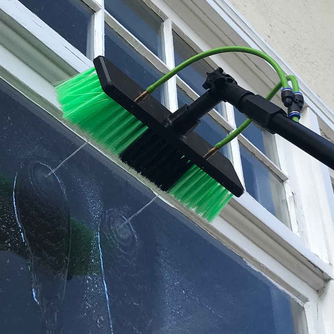 Close-up view of water fed pole, spraying the window with water using the water-fed pole's brush head nozzle.