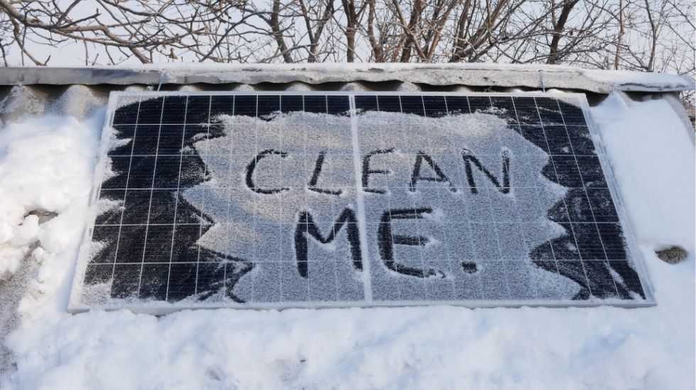 Snow-covered solar panel with 'Clean Me' written in the snow, highlighting the need for regular maintenance