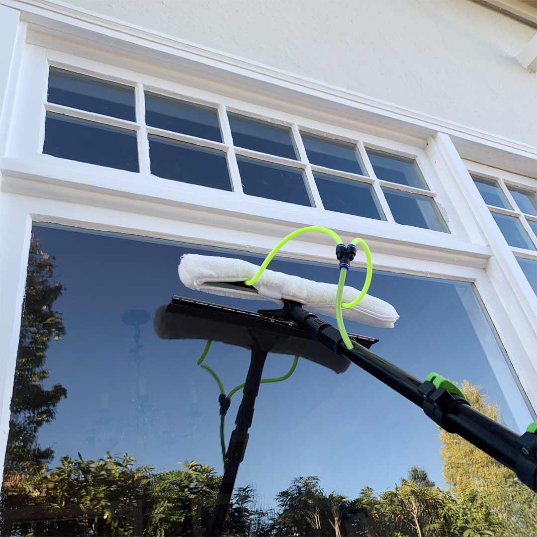 Side view of the All in One 2 Nozzle Scrubber & Squeegee attached to a water fed pole, in use for window cleaning.