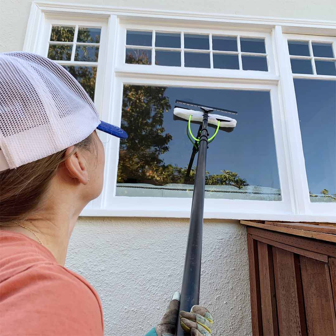 A woman cleaning a window using the All in One 2 Nozzle Scrubber & Squeegee.