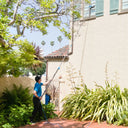 Fully extending a Venom water fed pole in a bright courtyard to clean high upper-level windows on a building with green shutters.
