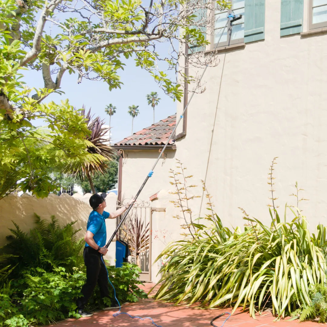Fully extending a Venom water fed pole in a bright courtyard to clean high upper-level windows on a building with green shutters.