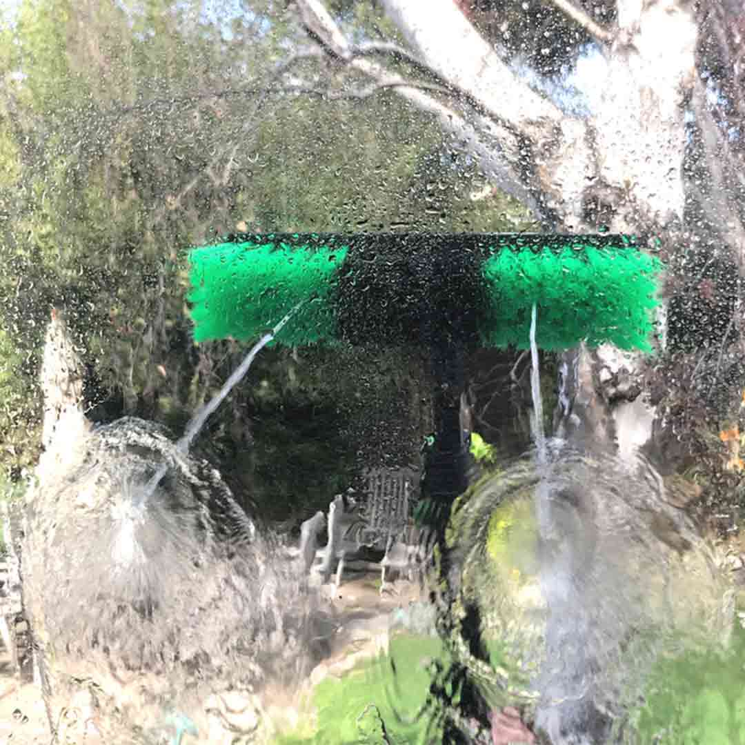Aluminum water-fed pole brush head nozzle spraying water on a glass window.